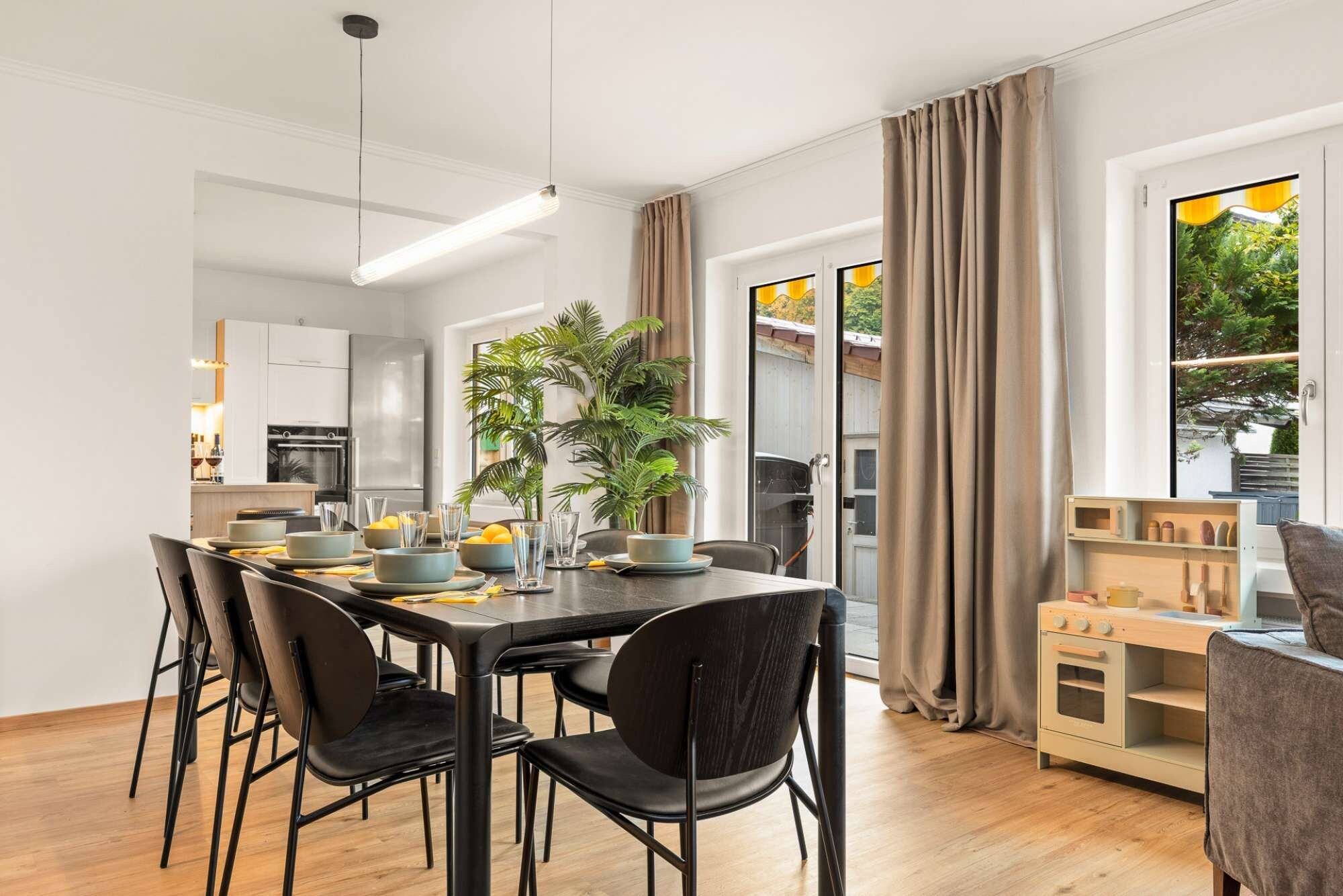 Un espace repas moderne avec une longue table, des chaises noires et une plante en pot.
