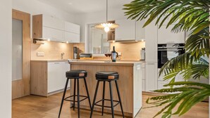Une cuisine moderne avec un plan de travail en bois, deux tabourets de bar, une bouteille de vin et une plante.