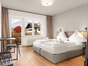 A hotel room with a bed, a desk, a chair, and a view of a mountain and a house. - Holiday home with terrace whirlpool, families welcome! (Ruhpolding)