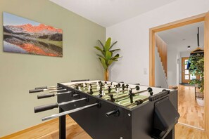 Una mesa de fútbol de mesa en una habitación con un cuadro en la pared, una planta y una escalera que lleva a otra zona.