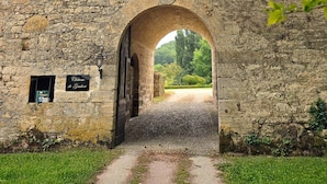 Un antiguo arco de piedra que da acceso a un camino, con un cartel que reza 'Chateau de Gaubert' y un farol en la pared.