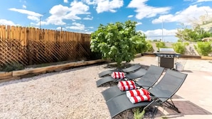 A patio area with lounge chairs and a grill, surrounded by a wooden fence and a tree. - Retro Vegas Getaway - Just 2 Miles to The Vegas Strip with a Pool & Hot Tub (Las Vegas)