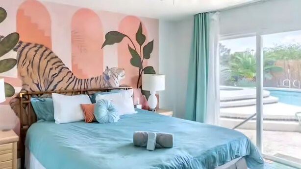 A bedroom with a bed, pillows, a nightstand, a lamp, and a view of a swimming pool. - Retro Vegas Getaway - Just 2 Miles to The Vegas Strip with a Pool & Hot Tub (Las Vegas)