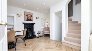Une pièce spacieuse dotée d’un parquet en bois à motifs en chevrons, d’une cheminée, d’un coin repas avec des chaises, d’un escalier et d’un tableau accroché au mur.