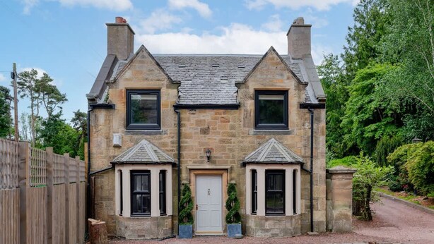 Une maison en pierre avec une porte centrale, deux fenêtres de chaque côté et une cheminée.