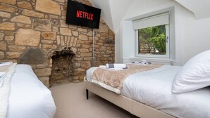 Une chambre avec un mur en pierre, une cheminée, un lit et un téléviseur fixé au mur qui affiche « NETFLIX ».