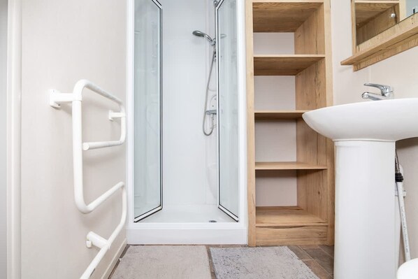 Une salle de bain avec une douche à parois de verre, un lavabo blanc et des étagères en bois.