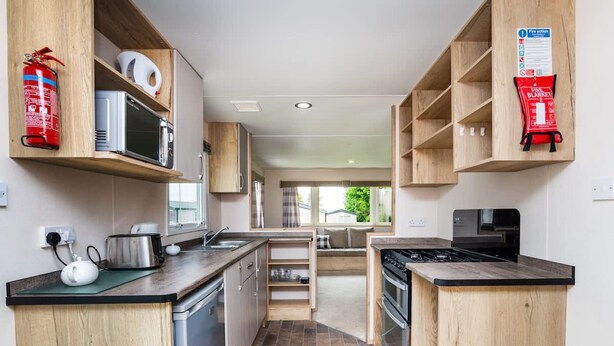 Una cucina compatta con mobili in legno, un forno a microonde, un piano cottura ed un estintore.