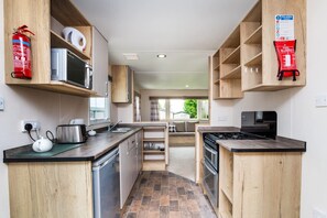 Une cuisine compacte avec des meubles en bois, un four à micro-ondes, une cuisinière et un extincteur.