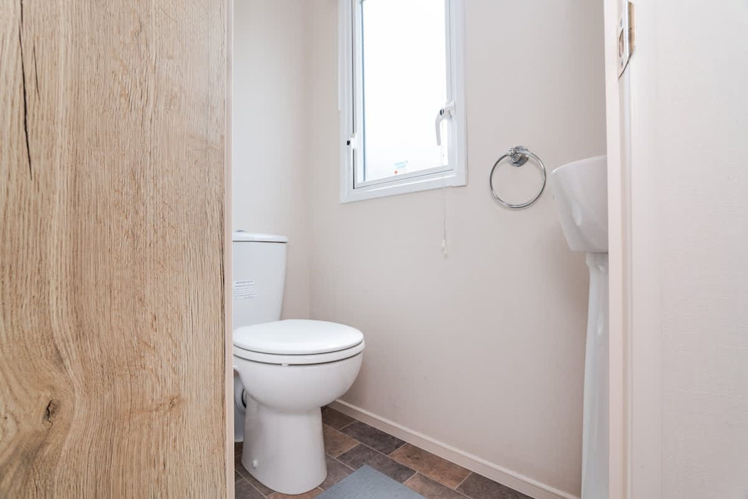Un baño pequeño y limpio con inodoro, ventana y toallero.