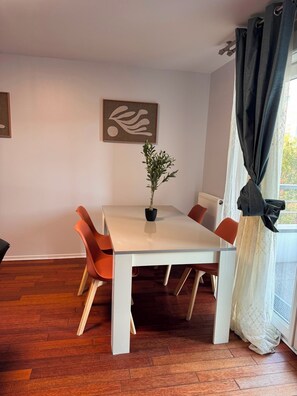 Ein Essbereich mit einem weißen Tisch, orangefarbenen Stühlen, einem Topfpflanzen und Kunstwerken an der Wand.