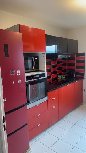 Una cocina pequeña con armarios rojos, un microondas, una estufa y una campana extractora negra.