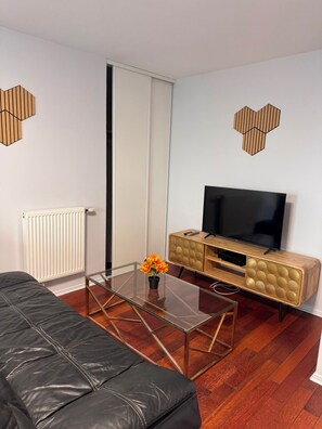 Ein modernes Wohnzimmer mit einer Ledersofa, einem Glastisch, einem Flachbildfernseher auf einer Holzkommode und einer Heizung.
