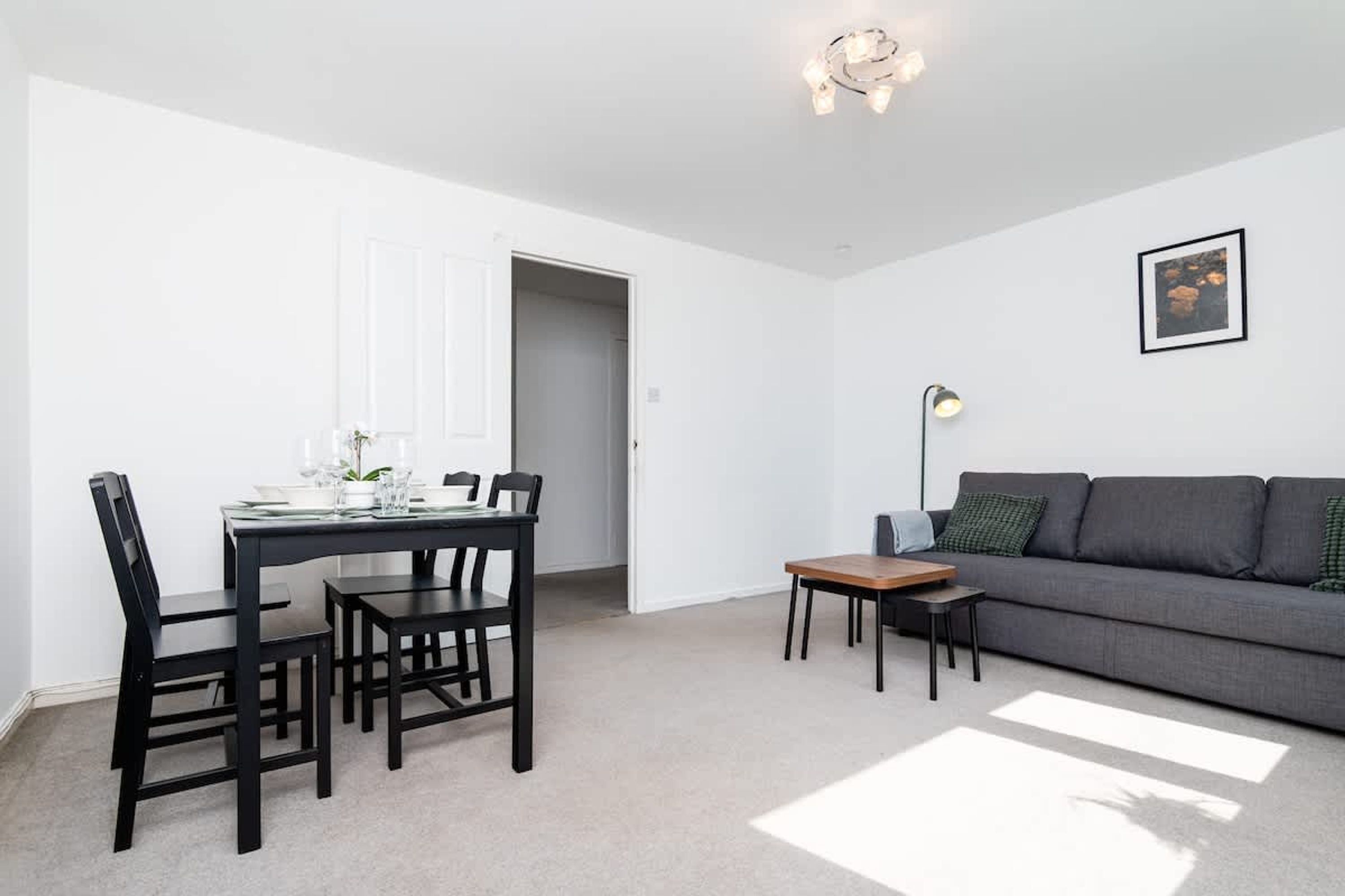 A modern living room with a grey sofa, a dining table with chairs, a small wooden table, and a floor lamp.