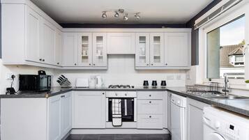 A modern kitchen with white cabinets, a built-in oven, a microwave, a coffee maker, and a washing machine.