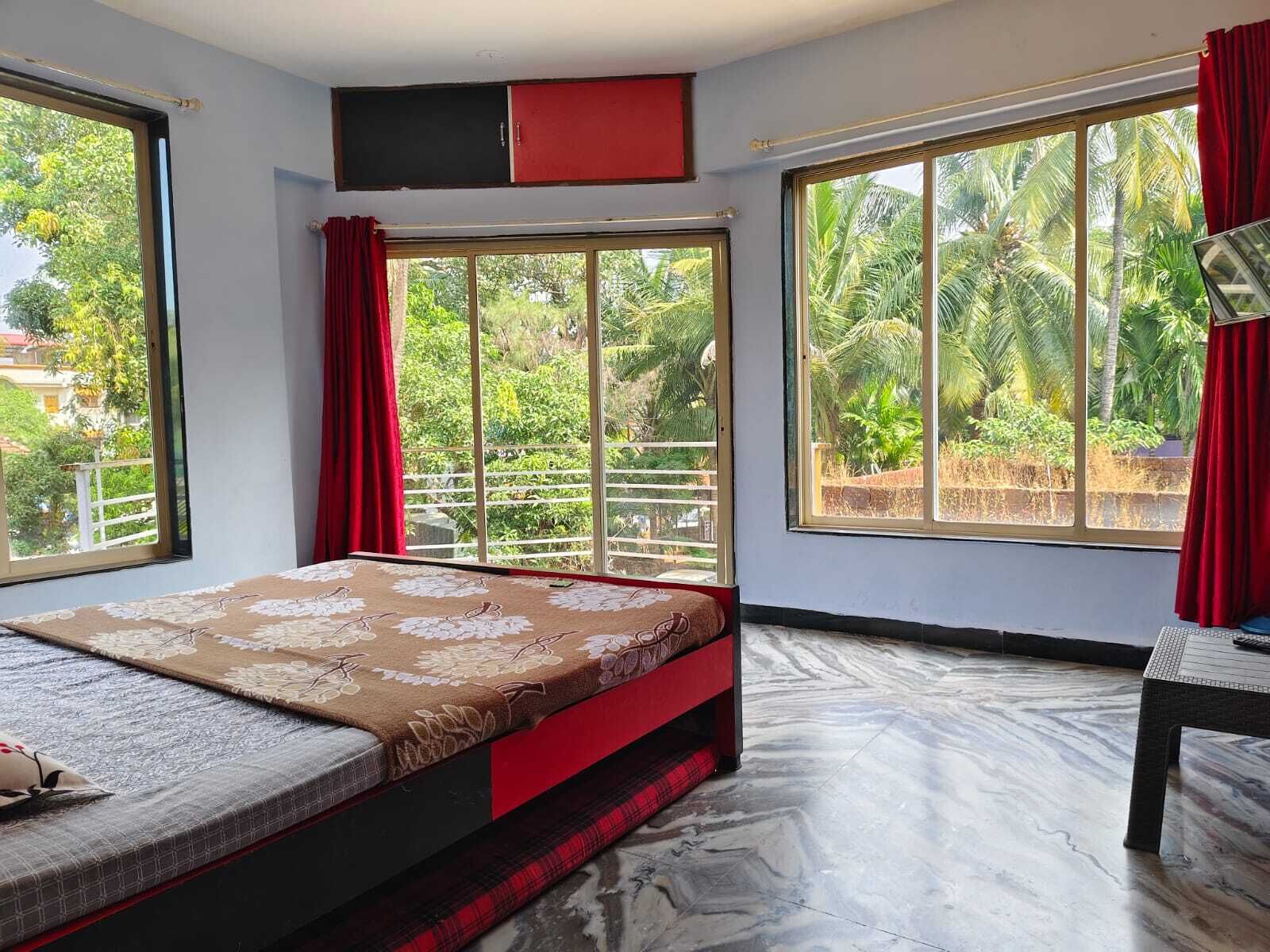 Ein Schlafzimmer mit Bett, Schreibtisch und großen Fenstern mit Blick auf Grünflächen.