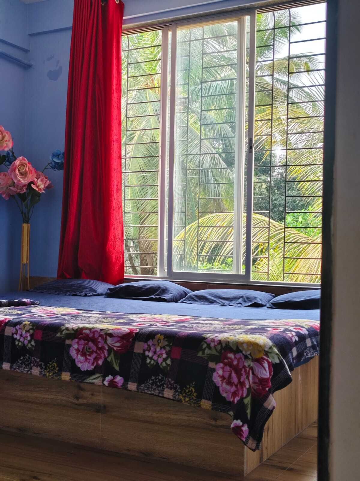 A bedroom with a bed, a window with a view of greenery, and a red curtain.