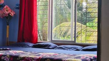 A bedroom with a bed, a window with a view of greenery, and a red curtain.