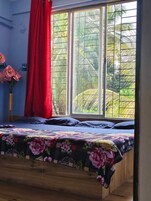 Quarto com uma cama, janela com vista para o verde e cortina vermelha.