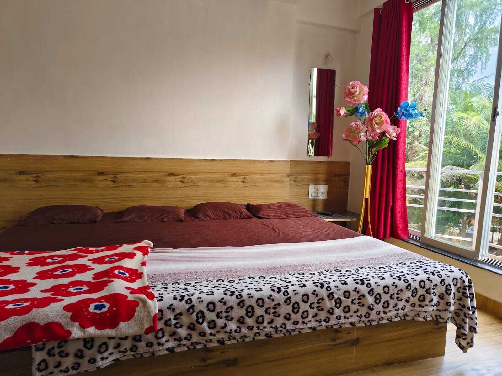 Un dormitorio con cabecera de madera, cama con ropa de cama roja, una manta de estampado de leopardo y una ventana con cortinas rojas y un jarrón de flores.