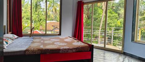 Une chambre avec un grand lit, deux fenêtres ornées de rideaux rouges et une vue sur la verdure environnante.