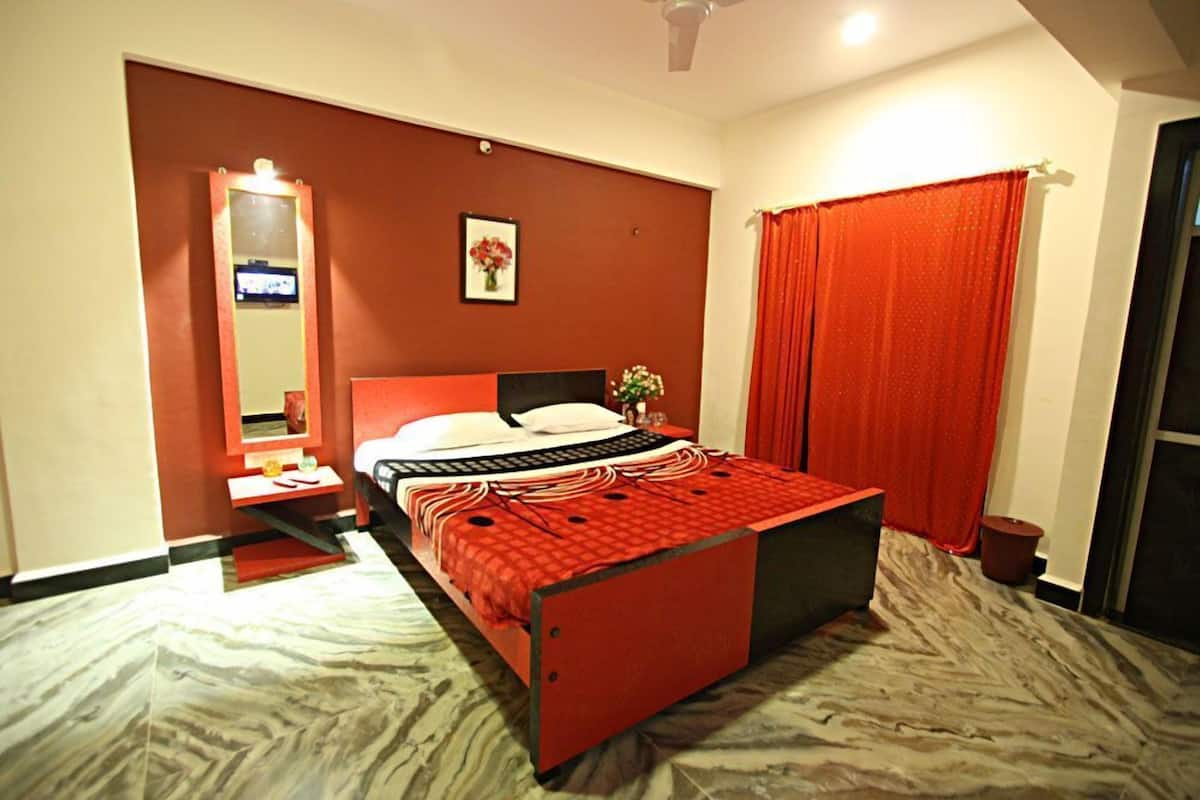A bedroom with a bed, a nightstand, a mirror, a red curtain, and a wall-mounted TV.
