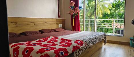 Quarto com uma cama grande, cabeceira de madeira, janela com vista para palmeiras e cortina vermelha.