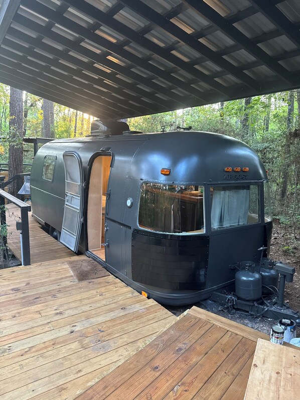 A black RV with a covered deck and a wooden exterior.