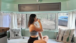 A person sitting on a bed in a camper with a sign reading "RESERVED FOR THE DOG" and a deer head decoration on the ceiling.