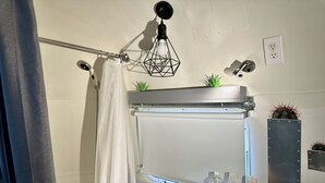 A bathroom with a shower curtain, a towel rack, a plant, and toiletries on the counter.