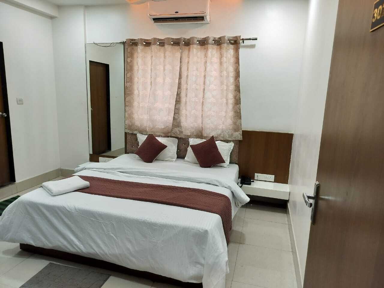 Quarto de hotel com cama, mesa de cabeceira, espelho e porta.