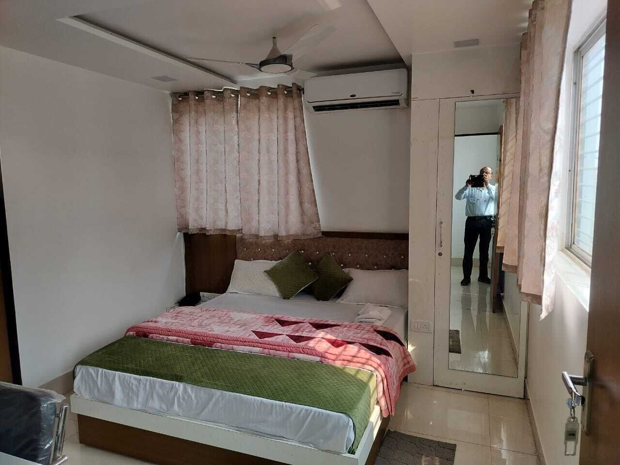 Un dormitorio con cama, ventilador de techo, aire acondicionado, espejo y ventana con cortinas.