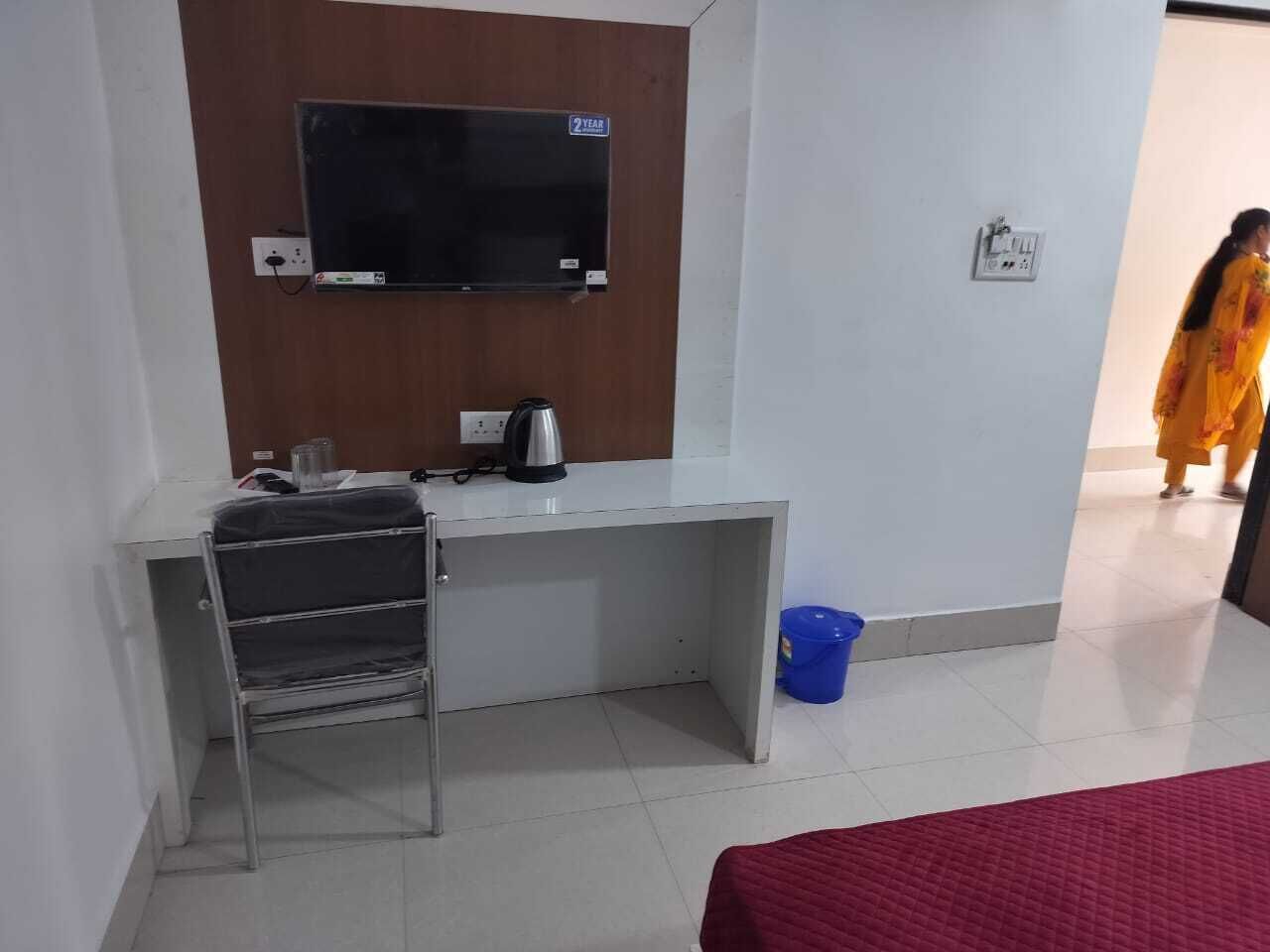 Una habitación de hotel con una cama, un escritorio con una silla, un televisor, un hervidor y un cubo azul.