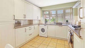 A kitchen with white cabinets, a washing machine, a sink, and a window with blinds. - Spacious 4 Bedroom House With Parking (Gateshead)