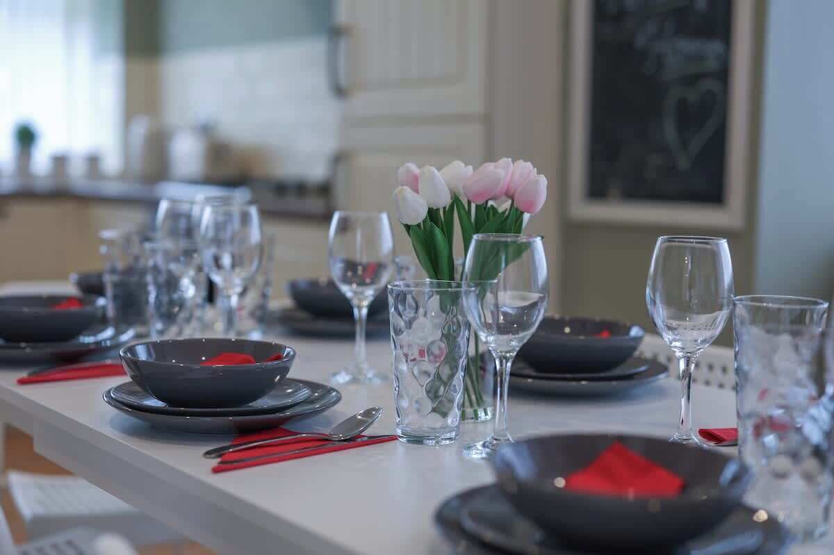 Een gedekte eettafel met borden, kommen, glazen en bestek, met een bloemenvaas in het midden.