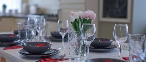 Una mesa de comedor dispuesta con platos, tazones, vasos y cubiertos, con un jarrón de flores en el centro.