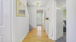 A hallway with white walls, a wooden floor, a mirror, a door with a glass panel, and a radiator. - Spacious 4 Bedroom House With Parking (Gateshead)