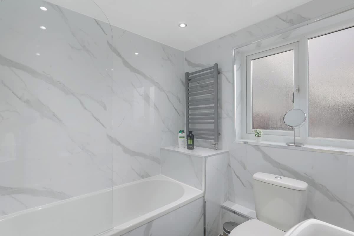 A modern bathroom with a marble floor, a bathtub, a toilet, and a window with a mirror.