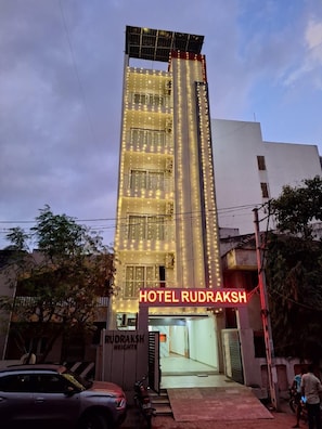 A hotel with a prominent vertical light display, a sign reading 'HOTEL RUDRAKSH,' and a gated entrance.