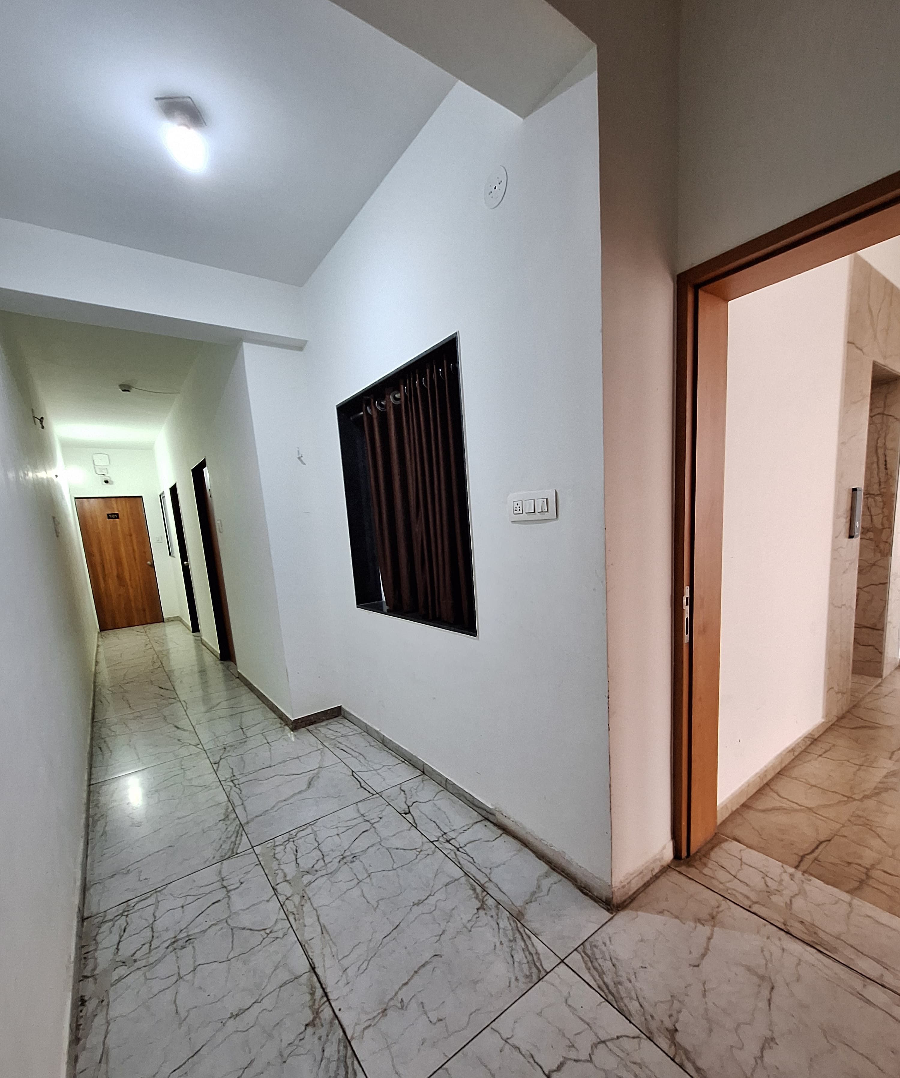 Un pasillo con piso de mármol, una ventana con cortinas y una puerta que da a otra habitación.