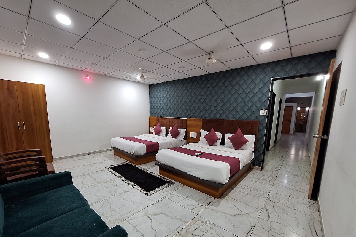 A hotel room with two beds, a wardrobe, a seating area, and a hallway.