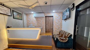 Zona de recepción de hotel con mostrador, un sofá, un reloj y un televisor montado en la pared.