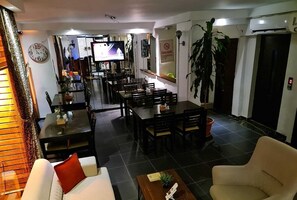 Rebedor d'hotel amb zona de dinar, un televisor que mostra un programa espacial, un rellotge i un senyalitzador que indica prohibició de fumar.