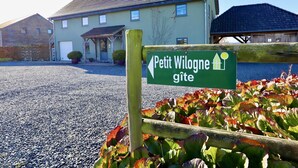 A sign for 'Petit Wilogne gîte' with a gravel driveway and a building in the background.