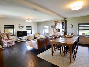 A living room with a sofa, a TV, a dining table with chairs, and a kitchen area with cabinets.