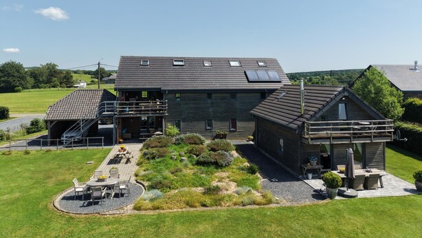 A modern house with a large patio, a covered outdoor seating area, and a small adjacent structure.