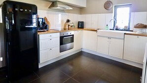 A modern kitchen with white cabinets, a black refrigerator, a wooden countertop, and a hanging light fixture.