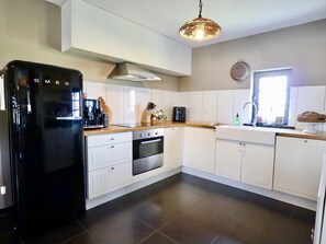 A modern kitchen with white cabinets, a black refrigerator, a wooden countertop, and a hanging light fixture.