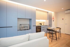 A modern kitchen with a built-in oven and microwave, a dining area with a table and chairs, and a living area with a sofa. - Liiiving in Porto - Campus Blue Studio (Porto)
