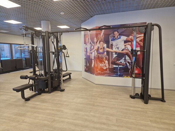 A gym with various exercise machines, a wall with a poster, and large windows. - Sport Hotel Kantri (Kankaanpää)